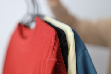 Three shirts hanging on a clothesline, one red, one yellow, and one blue. The person hanging the shirts is wearing a brown sweater
