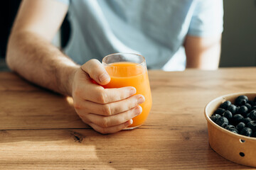 Glass of orange juice in male hand at home, close up.
