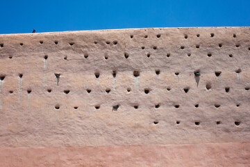 Pink beige medina wall in Marrakech with characteristic pigeon holes, some occupied by birds....