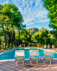 three white desk chairs or chaise lounge with blue swimming pool and hotel green garden on backgeound of vacation summer landscape