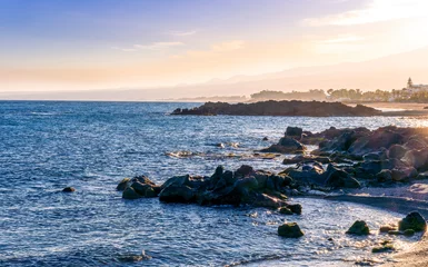 black rock sea beach during sunrise or sunset with golden sand, mild surf, blue calm water and beautiful cloudy sky with coast and mountains on background