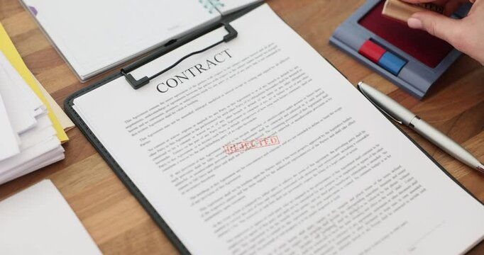 Businesswoman stamps rejected contract document on wooden desk. Woman clerk declines agreement terms marking document on clipboard in notary office