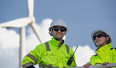 Maintenance engineer team standing at windmills at wind turbine farm. Group of people wear safety...
