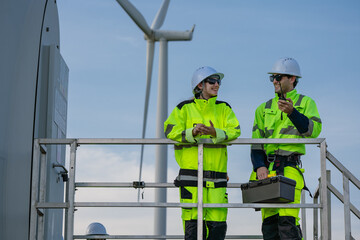 Maintenance engineer team standing at windmills at wind turbine farm. Group of people wear safety helmet and uniform working at alternative renewable energy wind station. Sustainable energy technology