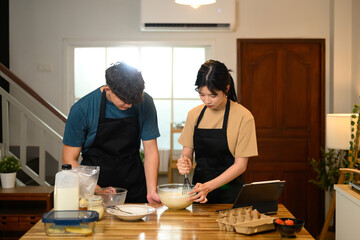 Happy couple in aprons following a recipe while making pancakes at home