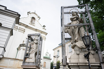 Historical statues encaged near a baroque church surrounded by greenery in Lviv, Ukraine.