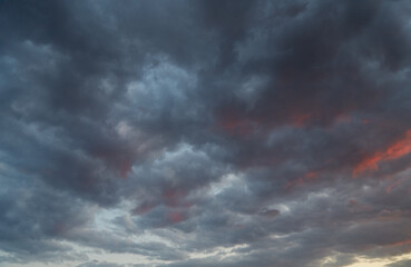 Stratocumulus clouds in the sky, wide celestial landscape with crimson highlights on black clouds—a harbinger of the elements, meteorology 