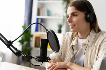 Young woman recording podcast in home studio using professional microphone and headphones