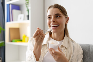 Happy woman eating yogurt at home with a spoon