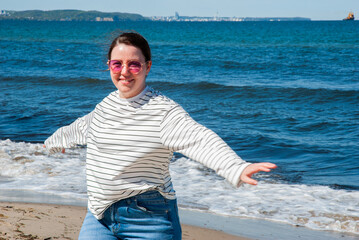 Young caucasian female enjoying a sunny beach day, wearing striped shirt and sunglasses, with arms...
