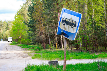 A skewed bus stop sign on the side of the road