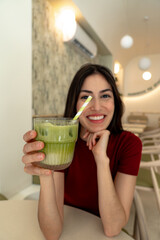 Happy customer savoring a refreshing iced matcha latte while sitting in a stylish modern cafe,...