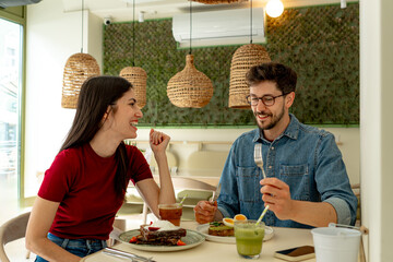 Happy couple enjoying a lively conversation and sharing laughter over a delicious brunch at a trendy, modern cafe with stylish decor