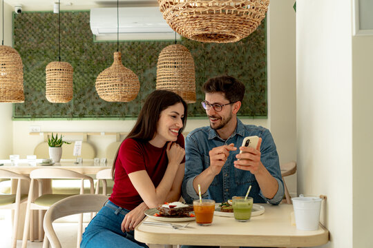 Man showing something funny on smartphone to his girlfriend while having breakfast in a modern restaurant