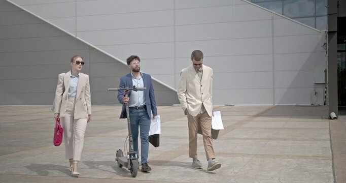 Businesspeople walk and discuss a project outdoors. One person holds an electric scooter while they talk and walk. - Powered by Adobe