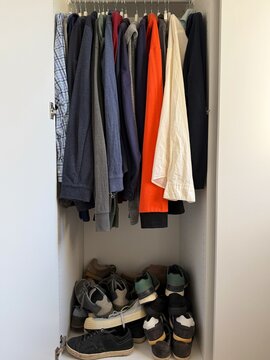 Close-up of a stack of men's shoes and assorted hoodies, shirts and sweatshirts hanging in a cupboard