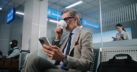 International Airport Terminal: Mature Businessman Sitting in Departure Lounge, Using Smartphone...