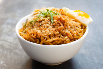 a bowl of instant noodles with toppings and an egg on a black background