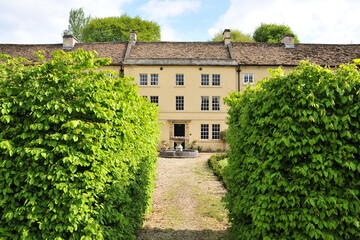 Green leaf hedgerow and garden path of a beautiful old mansion house on a street in an English village