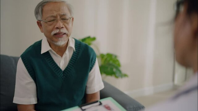 Elderly Asian man speaking seriously with female doctor during medical consultation at clinic. Seeking advice or diagnosis for health-related issues.