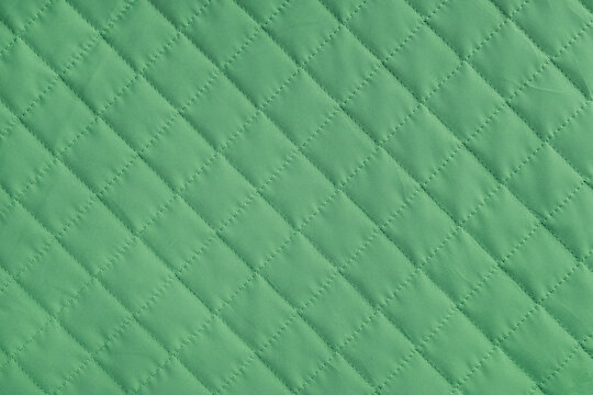 Checkered, diamond stitching pattern, green quilted fabric background. Blanket or puffer jacket, stitch rhombus texture close up, macro. Wallpaper, backdrop.