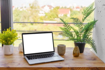 Laptop computer with white, transparent screen on wooden desk on wide window background. Office workspace, workplace in cafe or home. Mockup, template with copy space