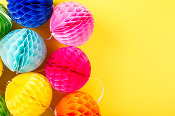 Festive yellow background with colorful paper balls. Greeting card concept for birthday, party, invitation, carnival. Copy space, top view, flat lay.