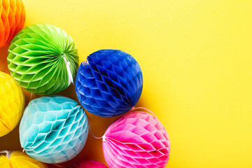 Festive yellow background with colorful paper balls. Greeting card concept for birthday, party, invitation, carnival. Copy space, top view, flat lay.