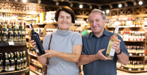 Mature couple choosing nice bottle of wine in supermarket