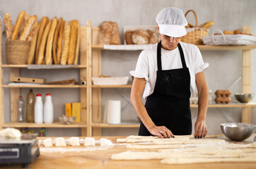 Elderly woman baker rolls out dough