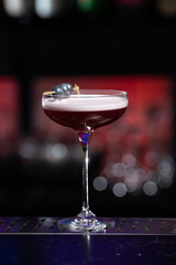 purple cocktail with a foamy white top is garnished with skewered blueberries on a textured bar surface