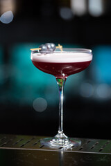 purple cocktail with a foamy white top is garnished with skewered blueberries on a textured bar surface