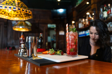 Strawberry cocktail sitting on bar with bartender preparing drinks in background