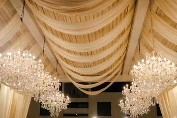 Elegant ceiling decor featuring draped fabric and ornate chandeliers. Perfect for a celebration,...
