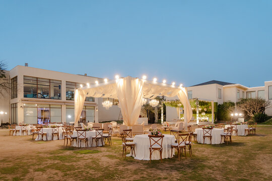 Outdoor Reception: Elegant event setup with draped canopy, round tables, and chandeliers under a twilight sky, perfect for celebrations.