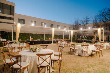 Outdoor event space with decorated tables and buffet under a canopy, ready for a celebration. ...