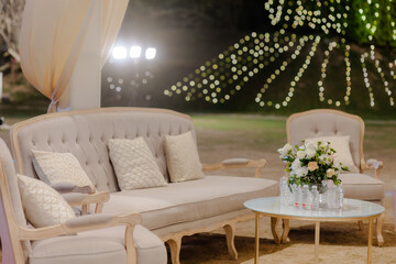 Elegant outdoor seating arrangement with a sofa, chairs, and floral centerpiece illuminated by soft lighting for a sophisticated event.
