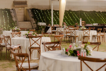 Elegant event space featuring round tables, cross-back chairs, and floral centerpieces, creating a warm and inviting atmosphere for celebrations.