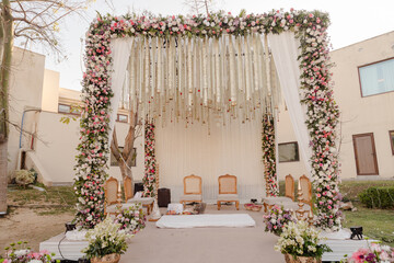 Elegant wedding setup with floral arch, draped fabric, and seating. Festive outdoor scene with soft colors and natural light for special event.