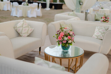 Elegant outdoor seating arrangement with white sofas and floral centerpiece on a gold table. Perfect for events and gatherings in a garden setting.