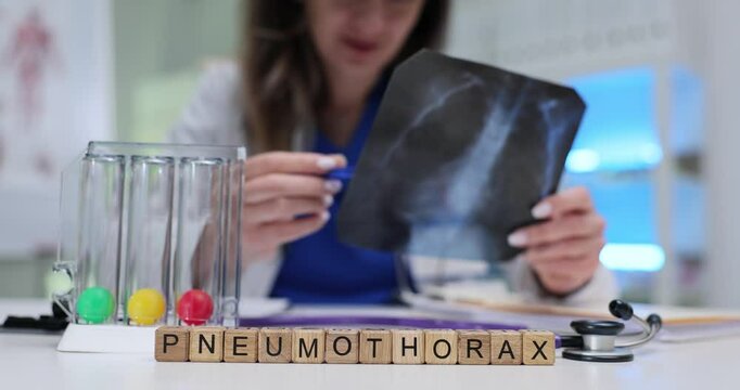 Word Pneumothorax on wooden blocks near incentive spirometer on doctor desk. Female pulmonologist holds lungs X-ray image in hospital slow motion