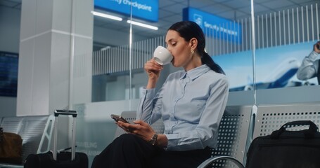 International Airport Terminal: Successful Businesswoman Using Smartphone and Drinking Coffee,...