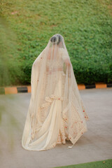 Elegant bride in traditional attire, a vision in cream with delicate veil. A moment captured in...