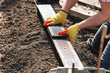 Construction worker actively installing plastic channel drainage system for future parking bay, using  hammer and  tools to adjust components