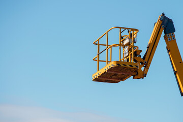 Elevated boom lift platform cherry picker against clear blue sky during daytime works on construction site with bright sunlight illuminating the machinery © Iryna