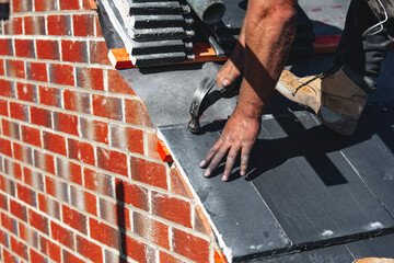Roofer carefully places roof tiles on a sloped surface while standing on top of a building under a...