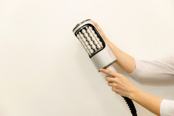 Close-up of a hand holding a modern anti-cellulite massage device used in professional cosmetic...