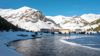 Panoramic image of the Nuria Valley with its monastery built in a snowy mountain valley, with a river.