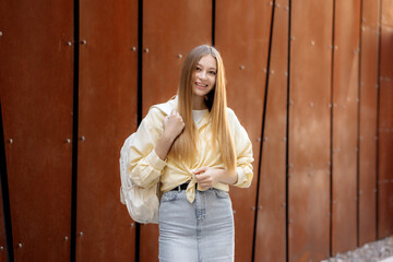 Young woman smiling with backpack in front of a modern brown wall during daytime in an urban setting