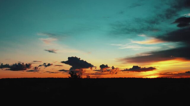 Evening sky at sunset background in forest. Dark clouds hanging above horizon. Majestic cloudscape in blue, orange, violet shades. Grey cloudlets bringing rain. Countryside skyline in twilight time